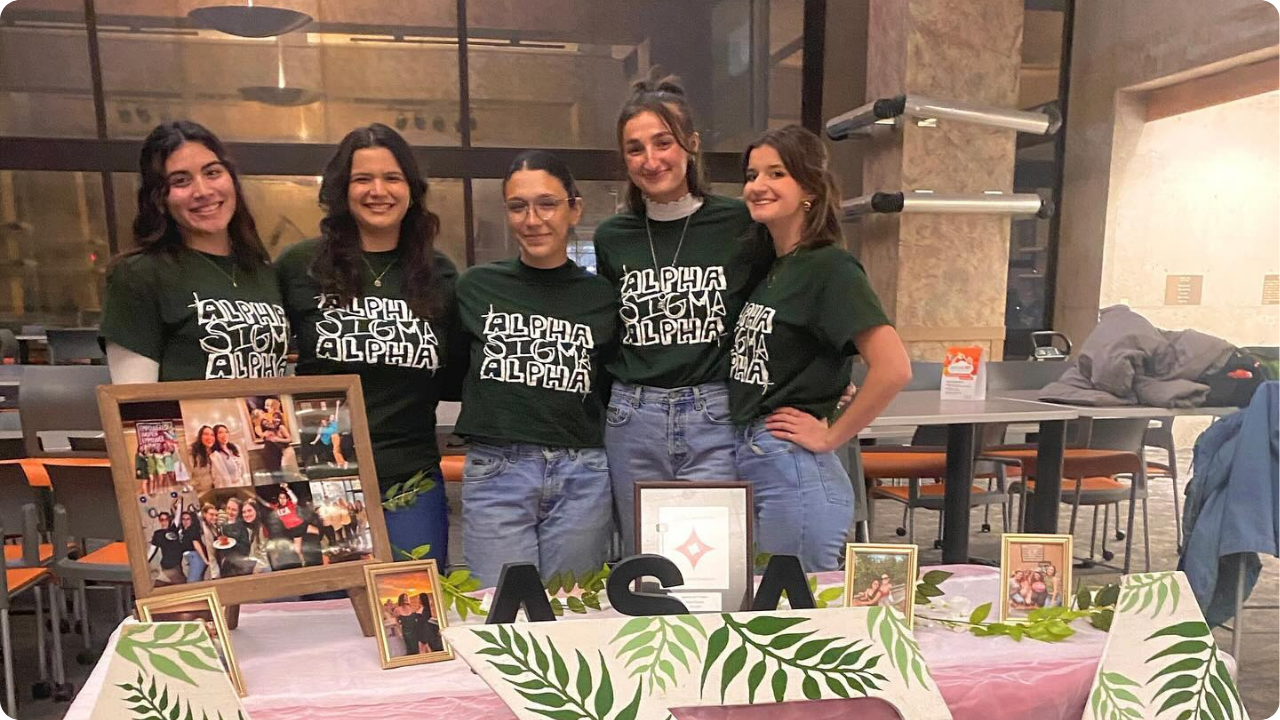 College girls wearing dark green custom shirts with white text at the back of a table.