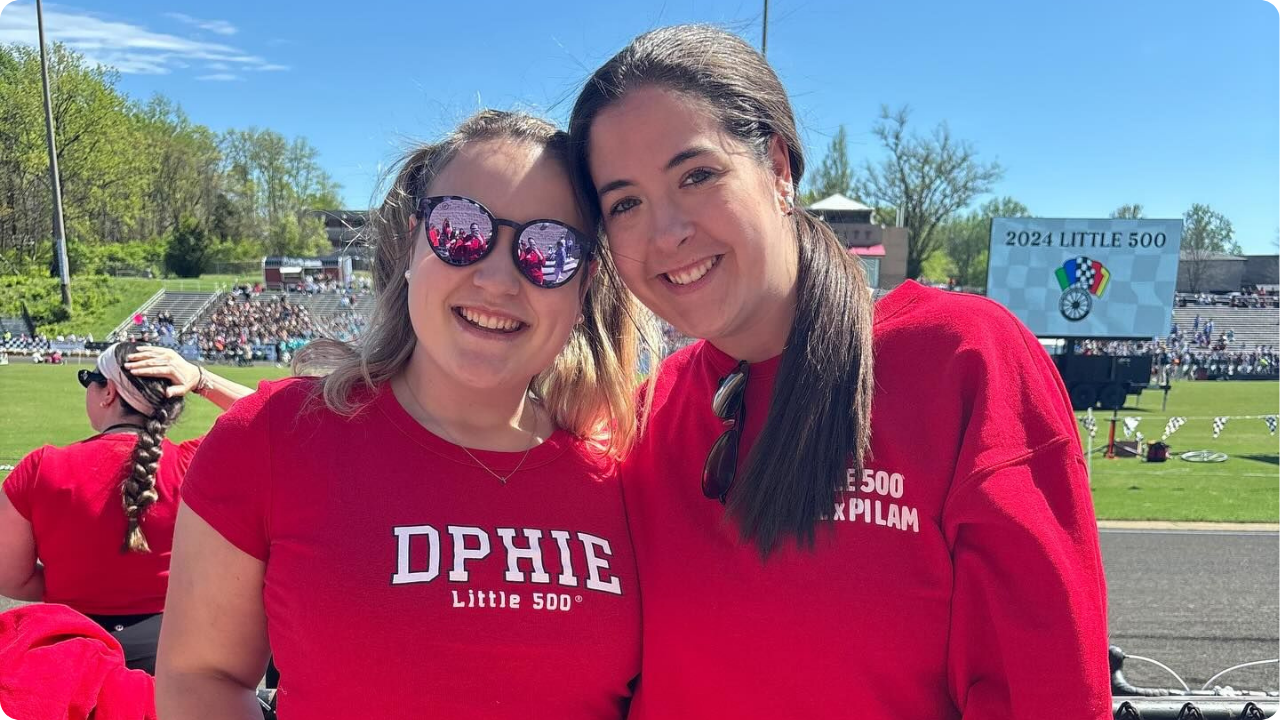 Delta Phi Epsilon sorority girls wearing red Big Little shirts at a stadium